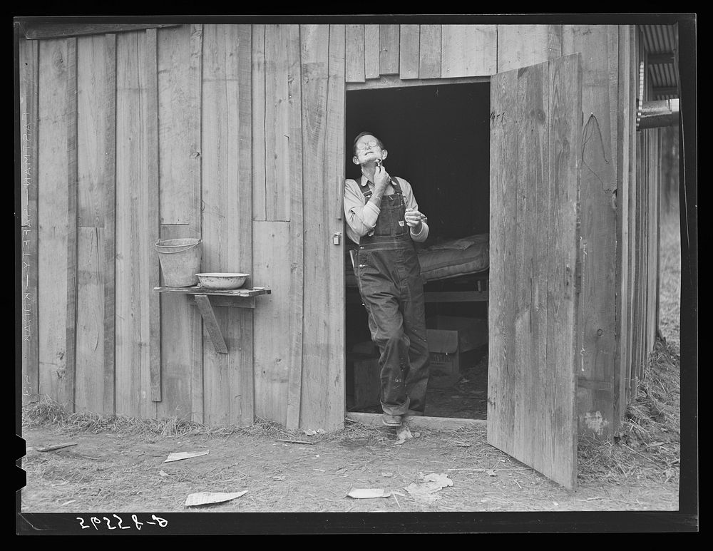 Charles B. Griggs shaving in front of his self-built shack on government property near Camp Livingston. He used to work on…