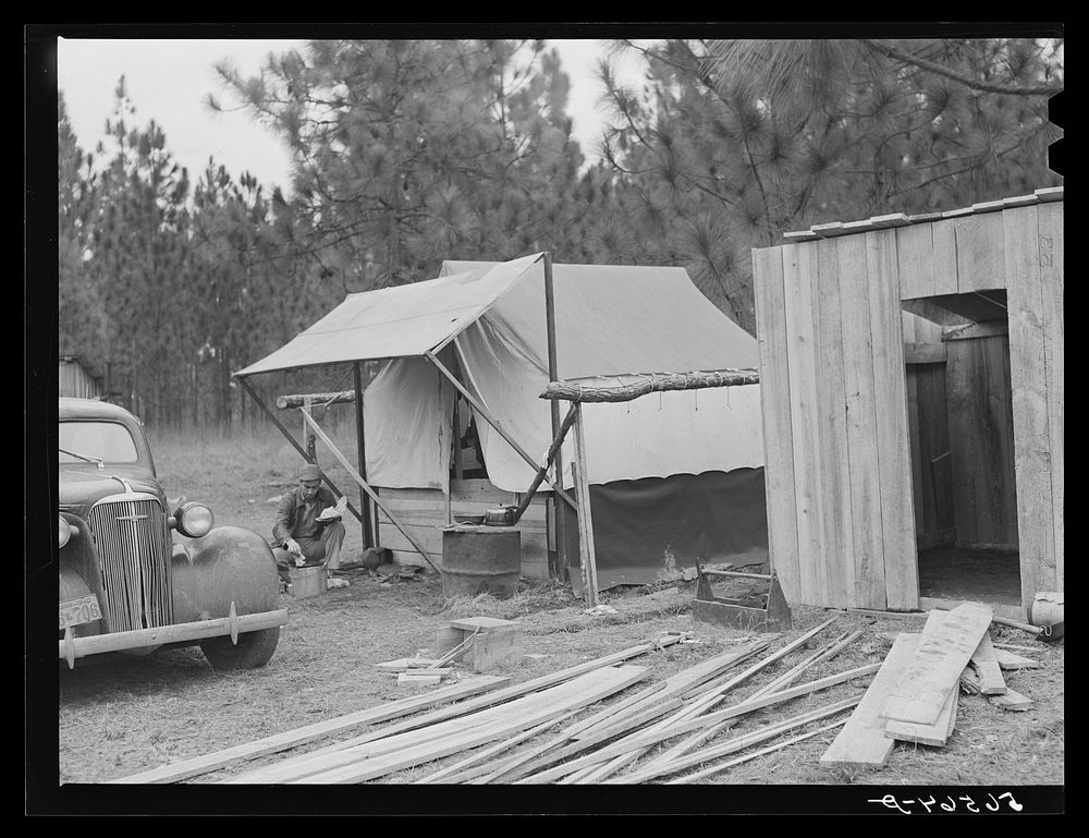 Camp Livingston construction worker cooking outdoors in front of shack which he built out of lumber he purchased or found…