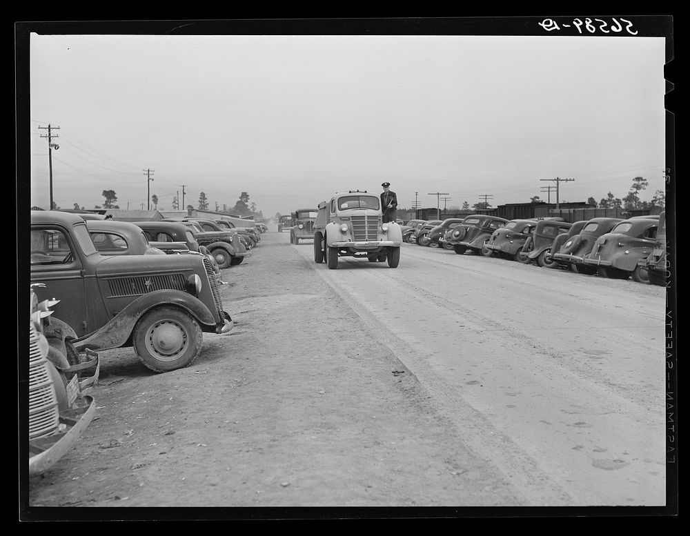 Cars of construction workers parked along highway by entrance to Camp Claiborne. Alexandria, Louisiana. Sourced from the…