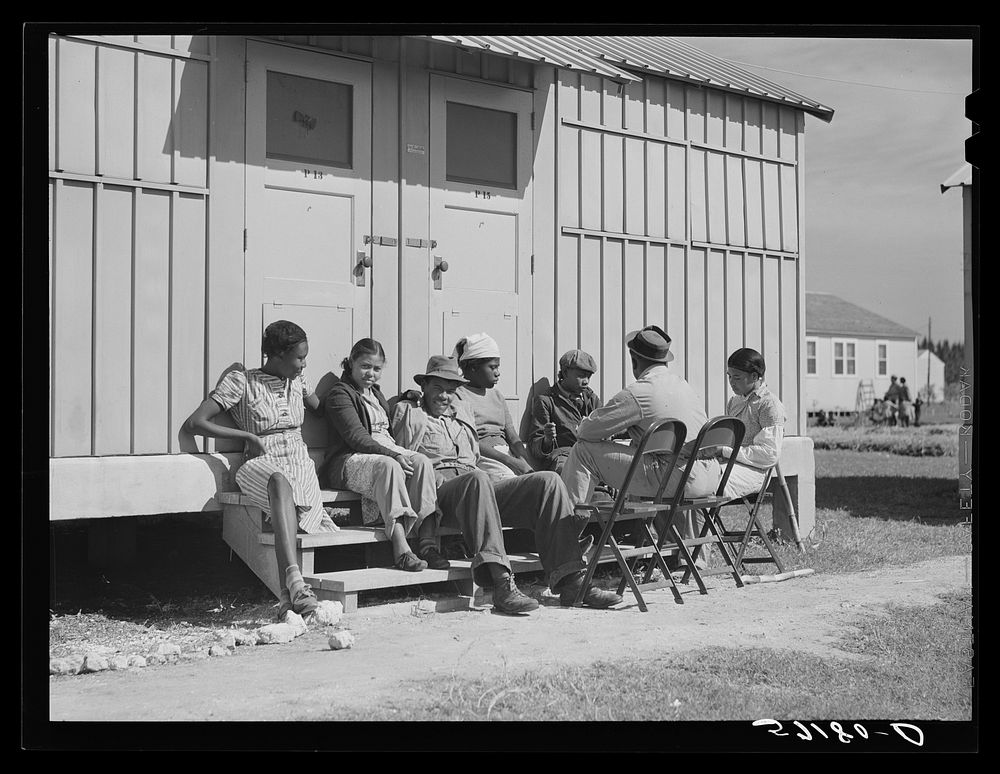 Agricultural workers in front of their metal shelters at Okeechobee migratory labor camp. Belle Glade, Florida. Sourced from…