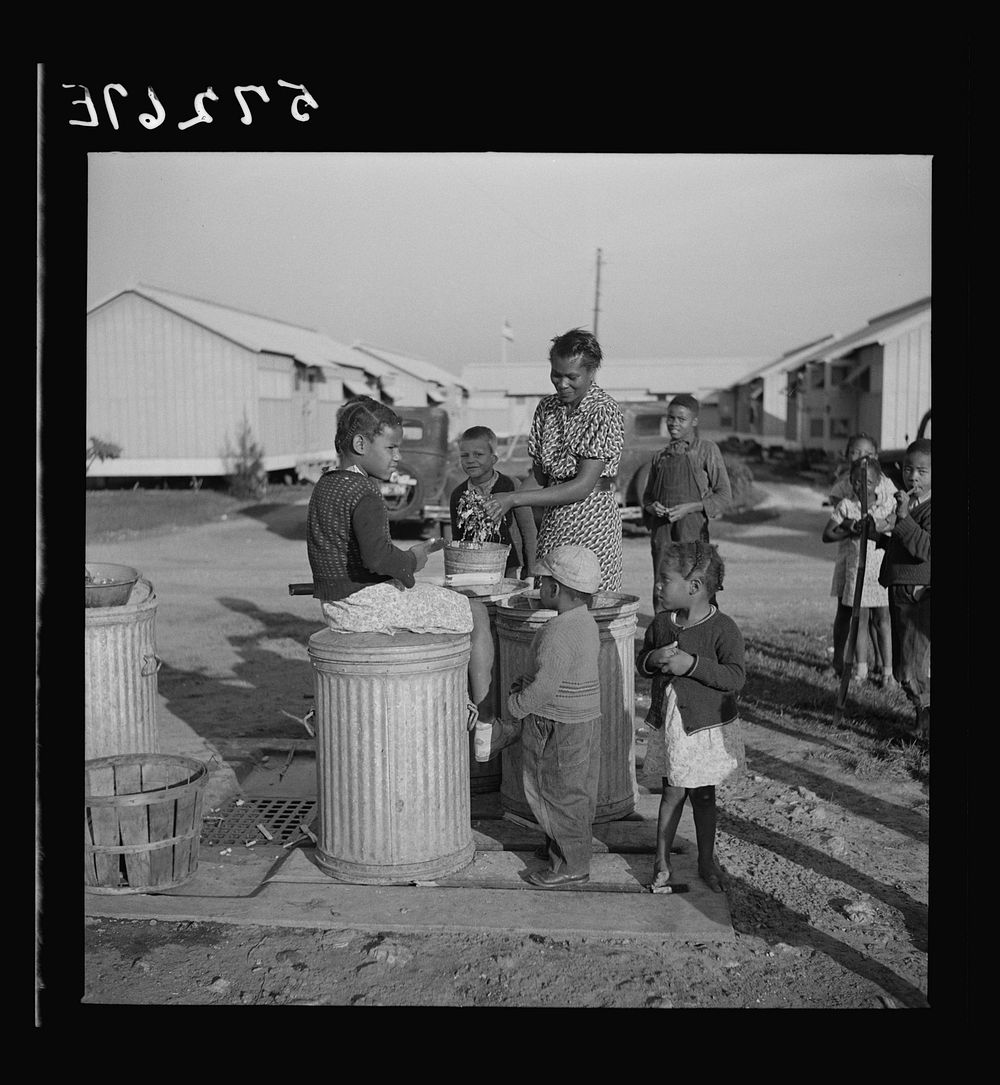 Washing greens by pump near metal shelters at Okeechobee migratory labor camp. Belle Glade, Florida. Sourced from the…