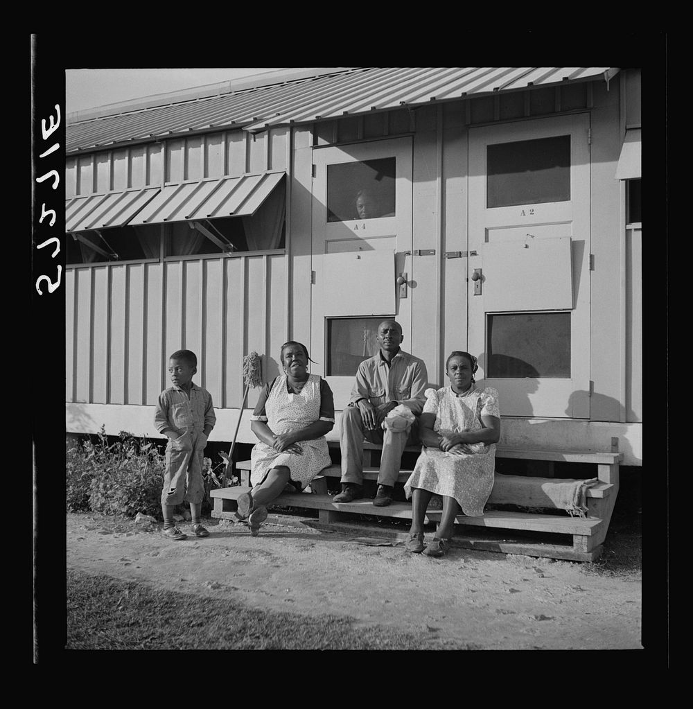 Migratory laborers sitting in front of their metal shelter at Okeechobee migratory labor camp. Belle Glade, Florida. Sourced…