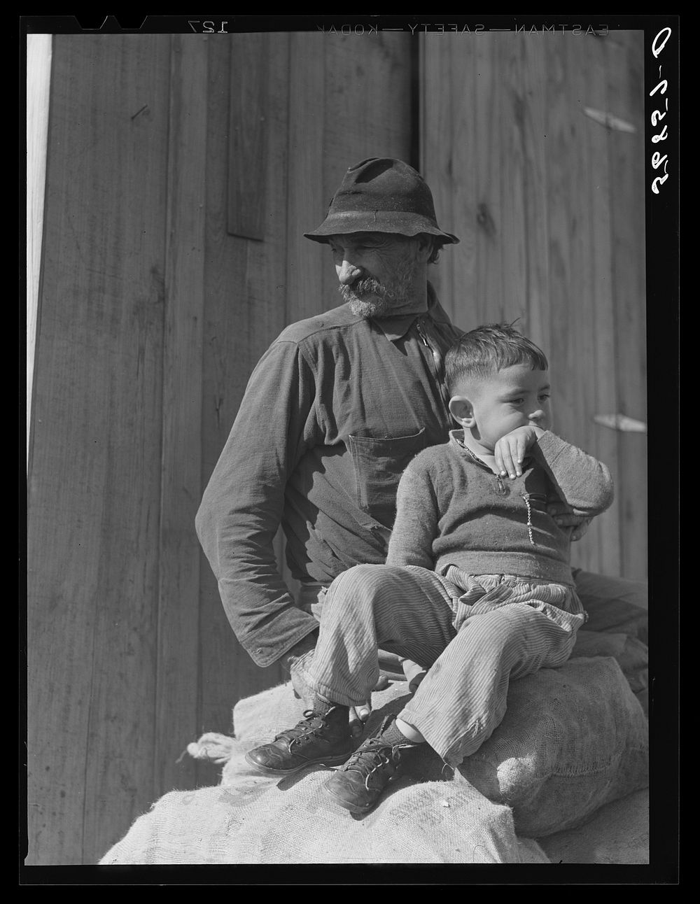 [Untitled photo, possibly related to: Spanish muskrat trapper and his grandson sitting on sacks of dried muskrat pelts, in…