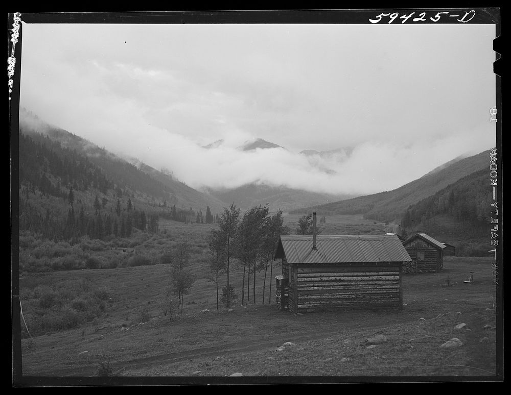 [Untitled photo, possibly related to: Cabins on ranch. Mist and clouds over mountains before an early blizzard]. Sourced…