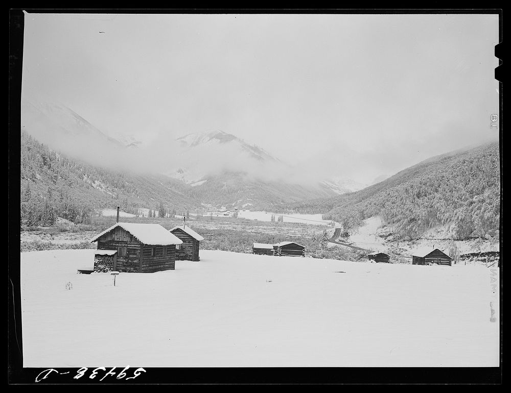 [Untitled photo, possibly related to: Cabins on ranch. Mist and clouds over mountains before an early blizzard]. Sourced…