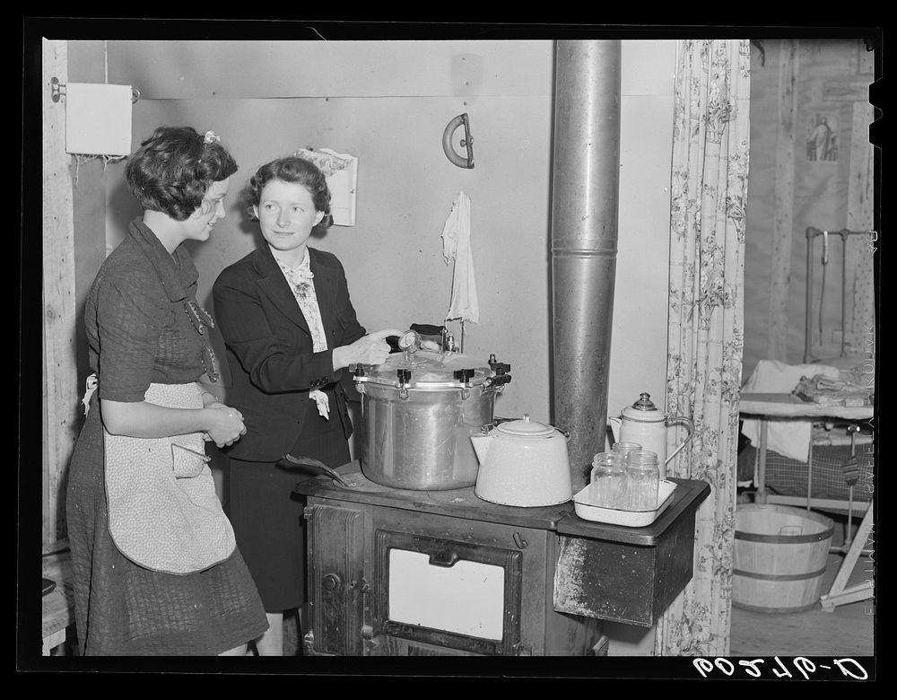 Home supervisor demonstrating use of pressure cooker to wife of rehabilitation borrower. Chippewa County, Wisconsin. Sourced…