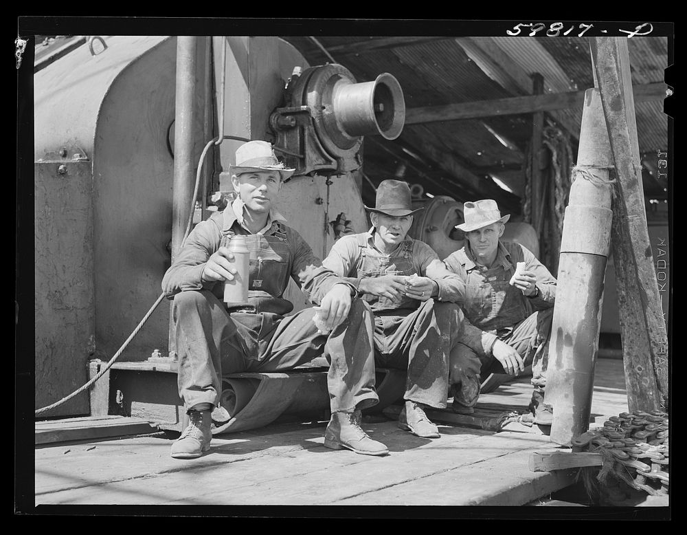 C.L. Saxton, driller; J.G. Betz, Cathead man; and L.C. Westerman, eating lunch around oil well in C.C. Graber pool of…