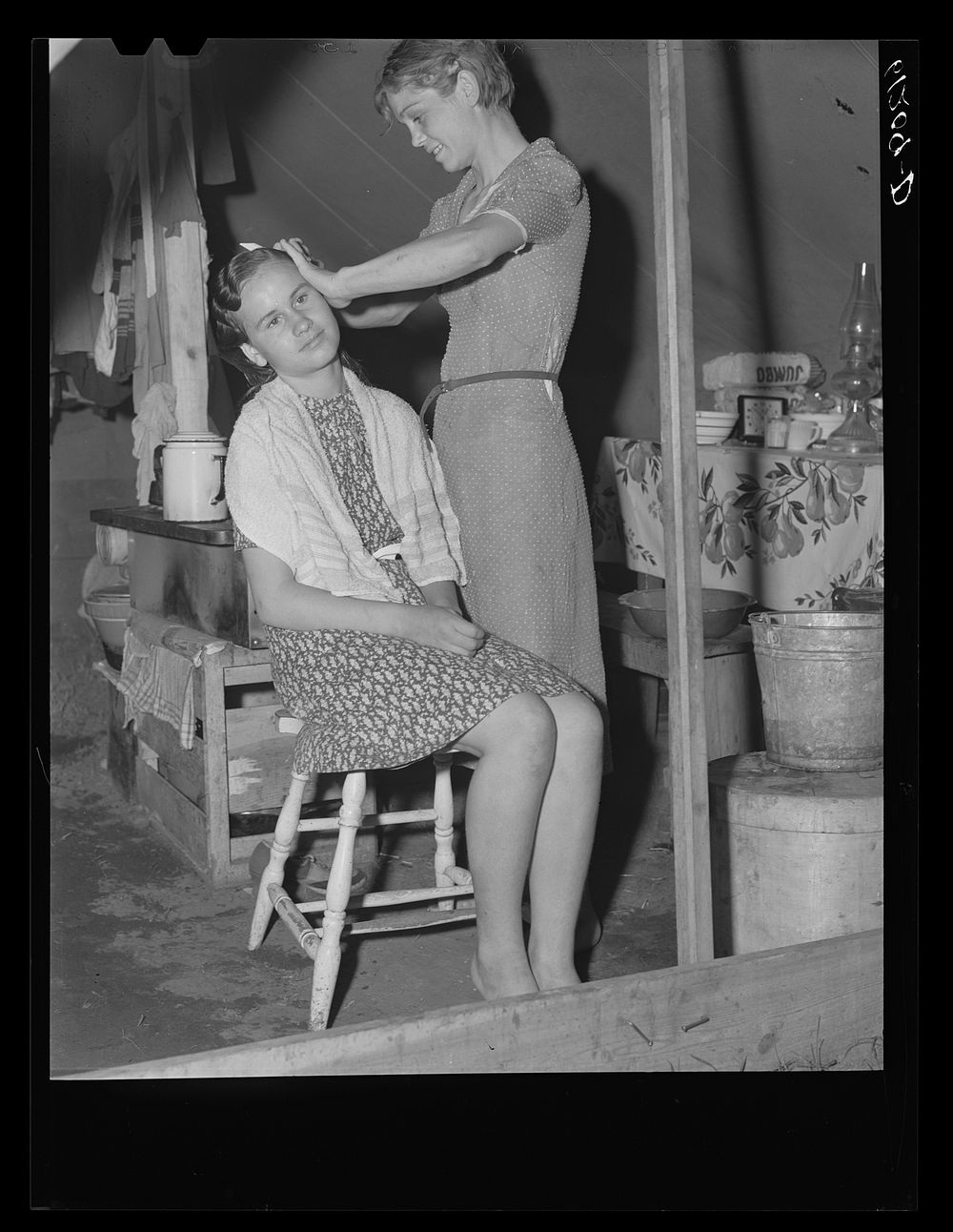 Migrant girl fixing her sister's hair. Roadside camp of fruit worker. Berrien County, Michigan. Sourced from the Library of…