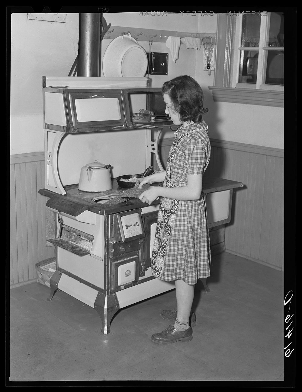 Farm girl putting wood in kitchen stove. Meeker County, Minnesota. Sourced from the Library of Congress.