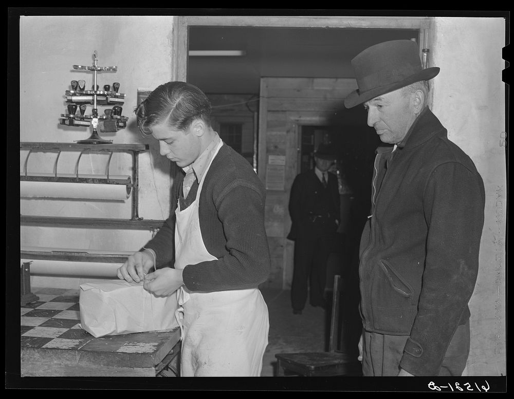 Wrapping up a roast from cold storage locker for farmer to take home. Casselton, North Dakota. Sourced from the Library of…