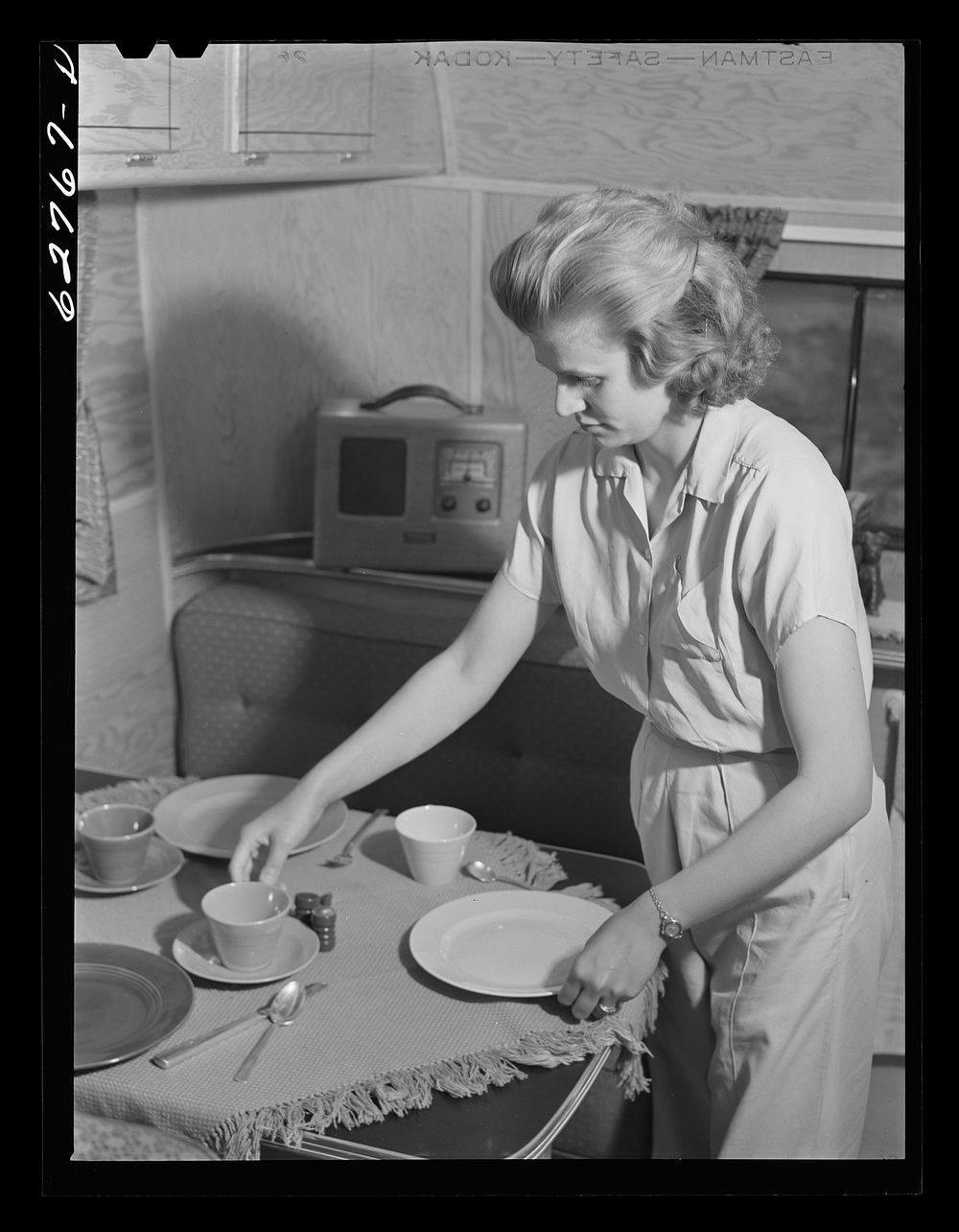 Wife of defense worker setting table for dinner in trailer home. Trailer camp at Erie, Pennsylvania. Sourced from the…