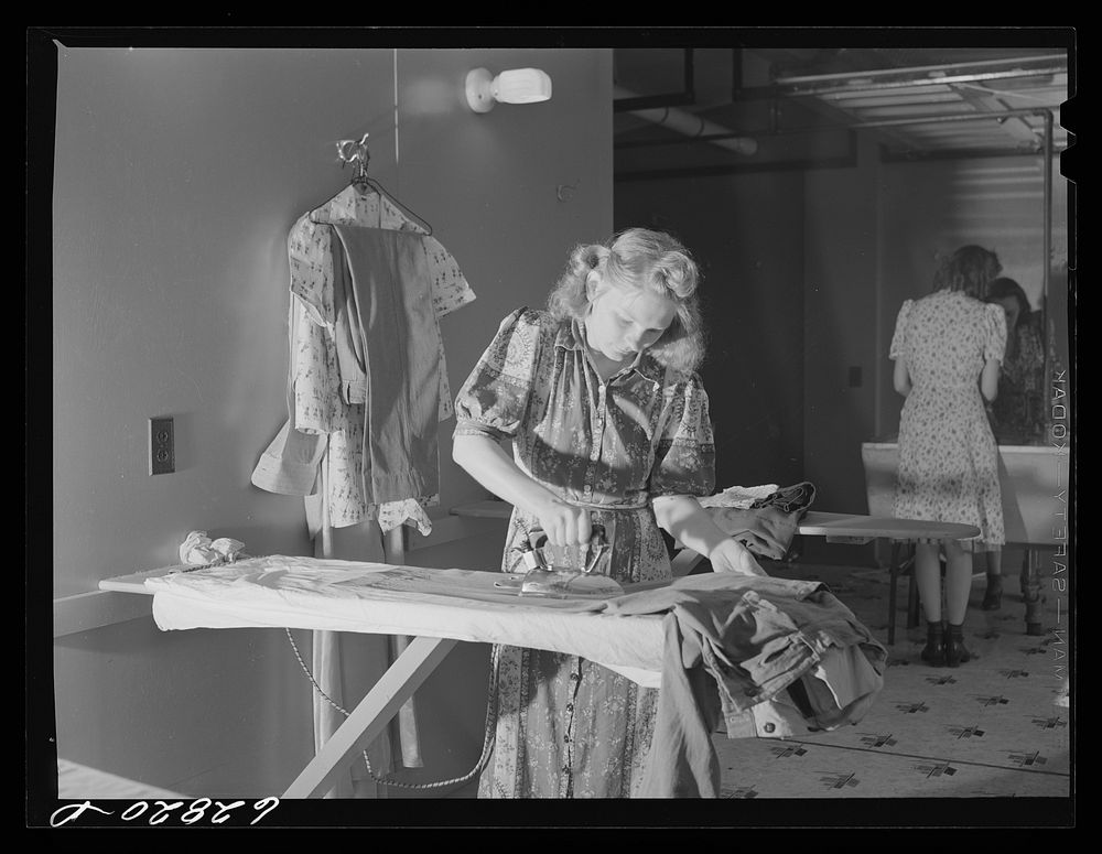 Wife of defense worker ironing clothes in utility building at FSA (Farm Security Administration) trailer camp. Erie…