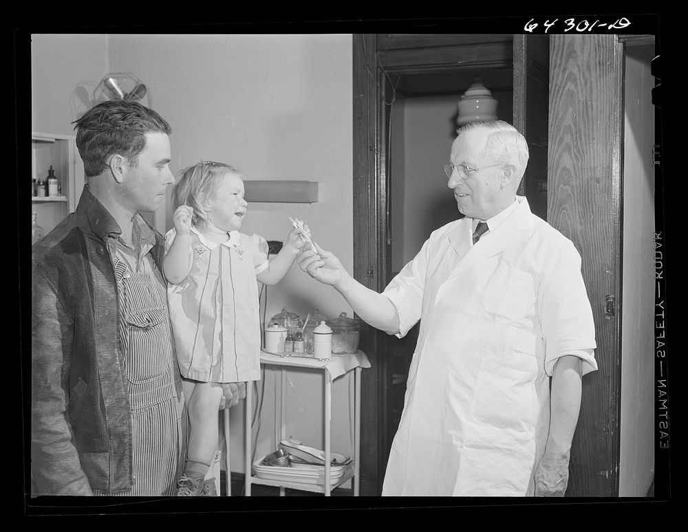 Chaffee, Missouri. Doctor giving little girl a stick of candy. She has just received an injection of anti-hydrophobia…