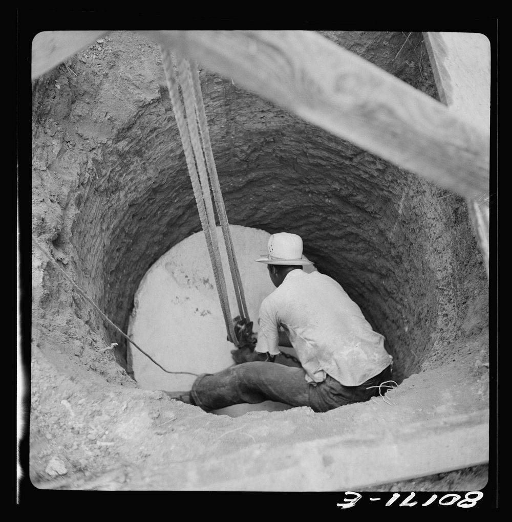 The cement well cap is lowered down the cleared well with a two purchase block and tackle. John Hardesty well project…