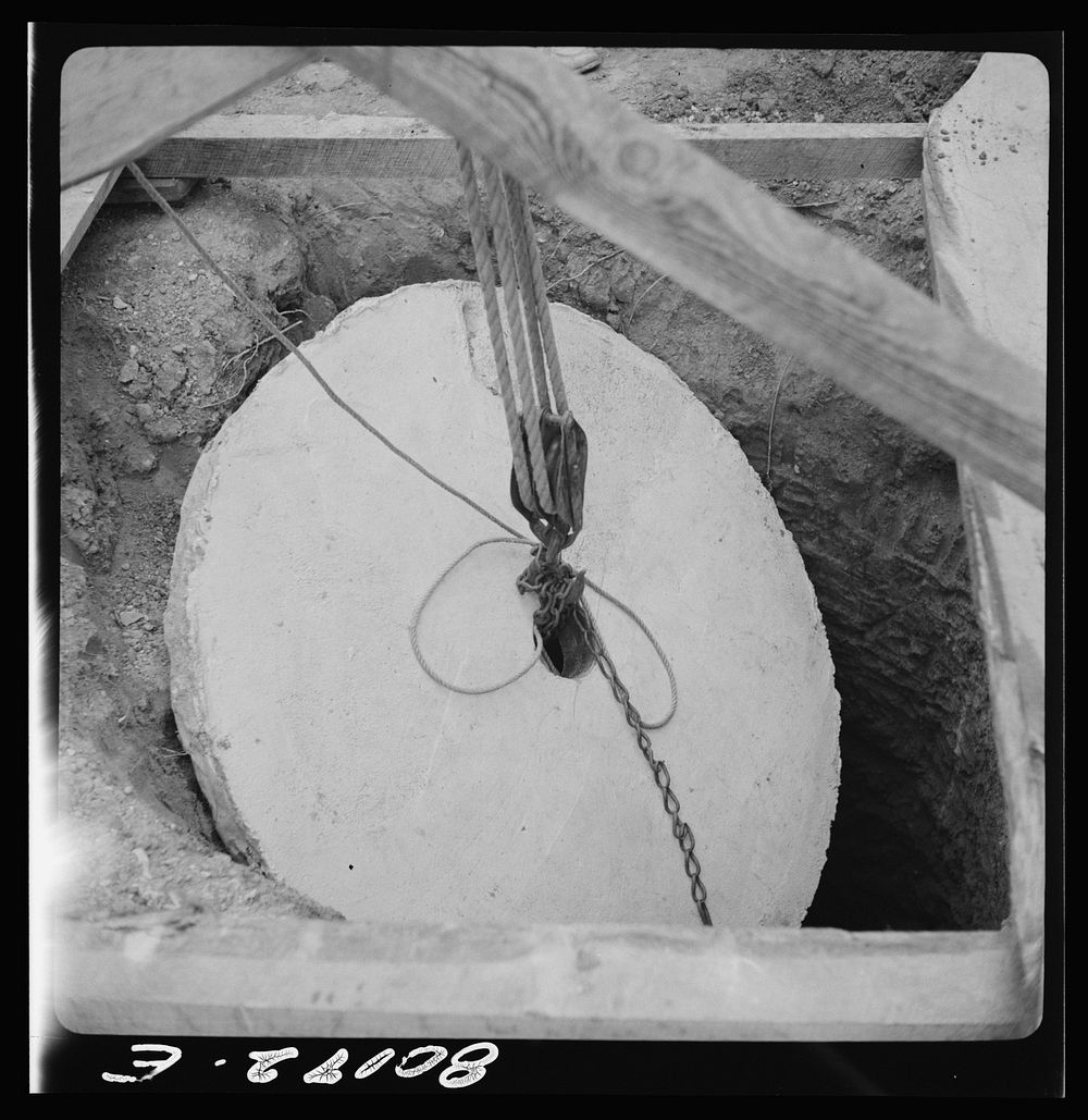 Block and tackle hung from windlass serve as a rig to lower cement cap into place. John Hardesty well project, Charles…