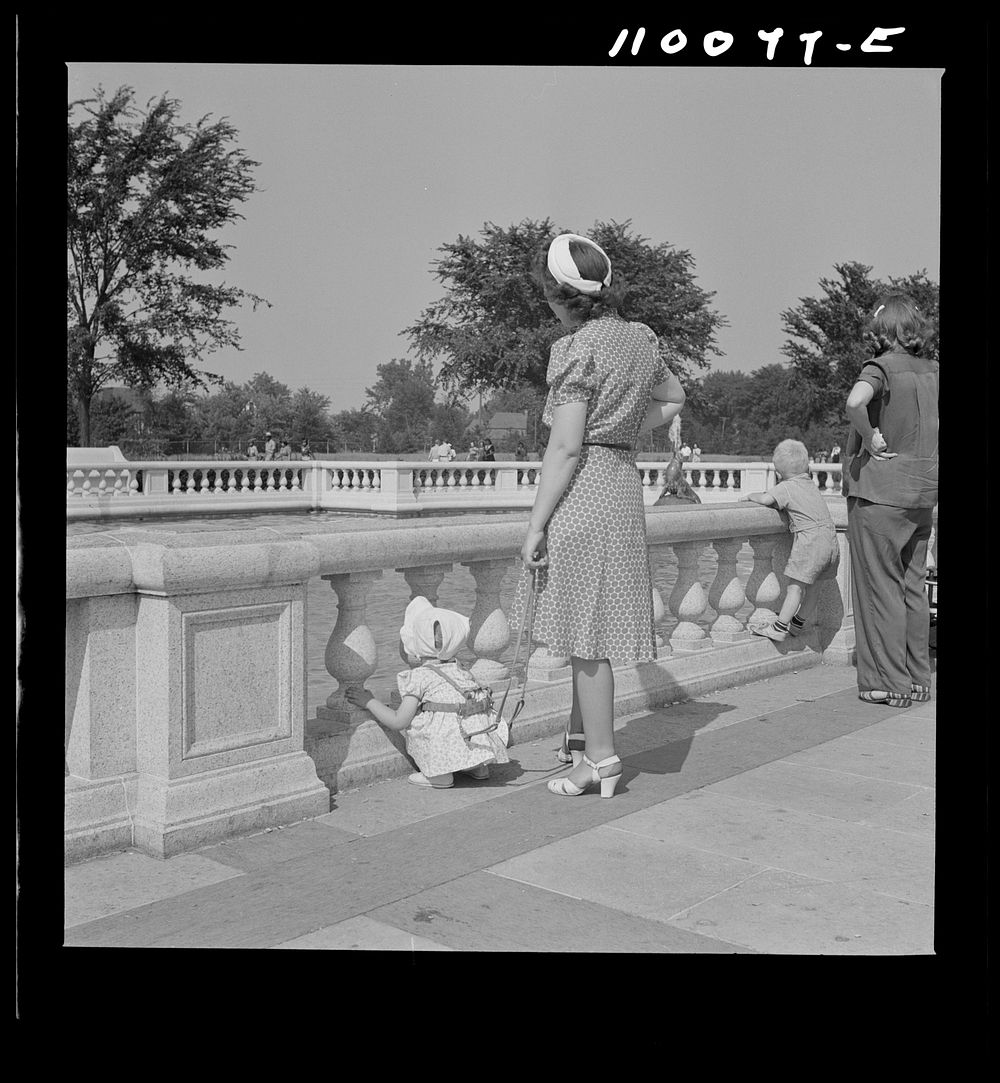 Detroit, Michigan. Woman adjusting a harness strap to prevent child from getting lost in zoological park. Sourced from the…