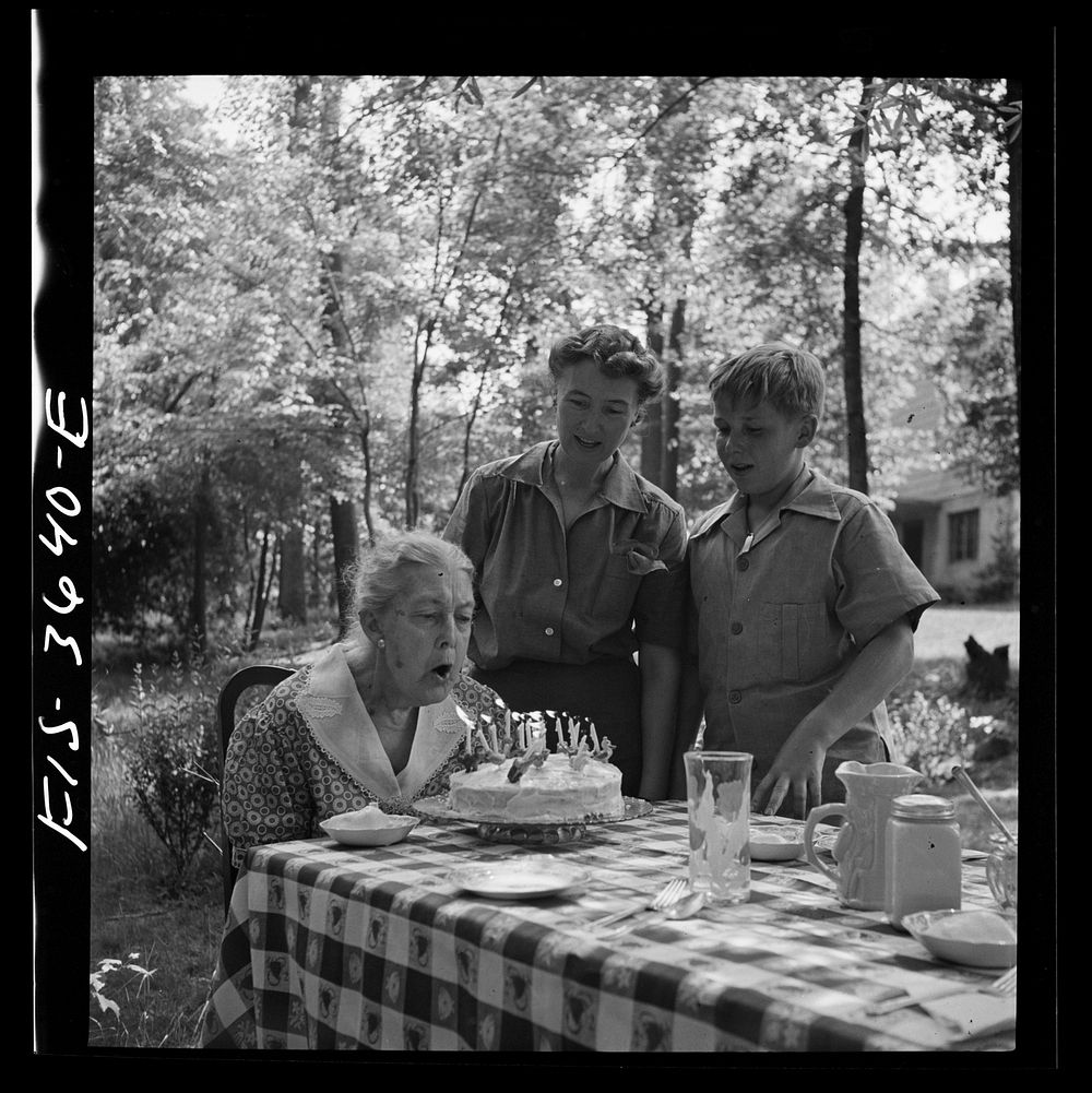Greenbelt, Maryland. Grandma Taylor blows out the candles on her eighty-third birthday cake while her daughter, Mrs. McCarl…