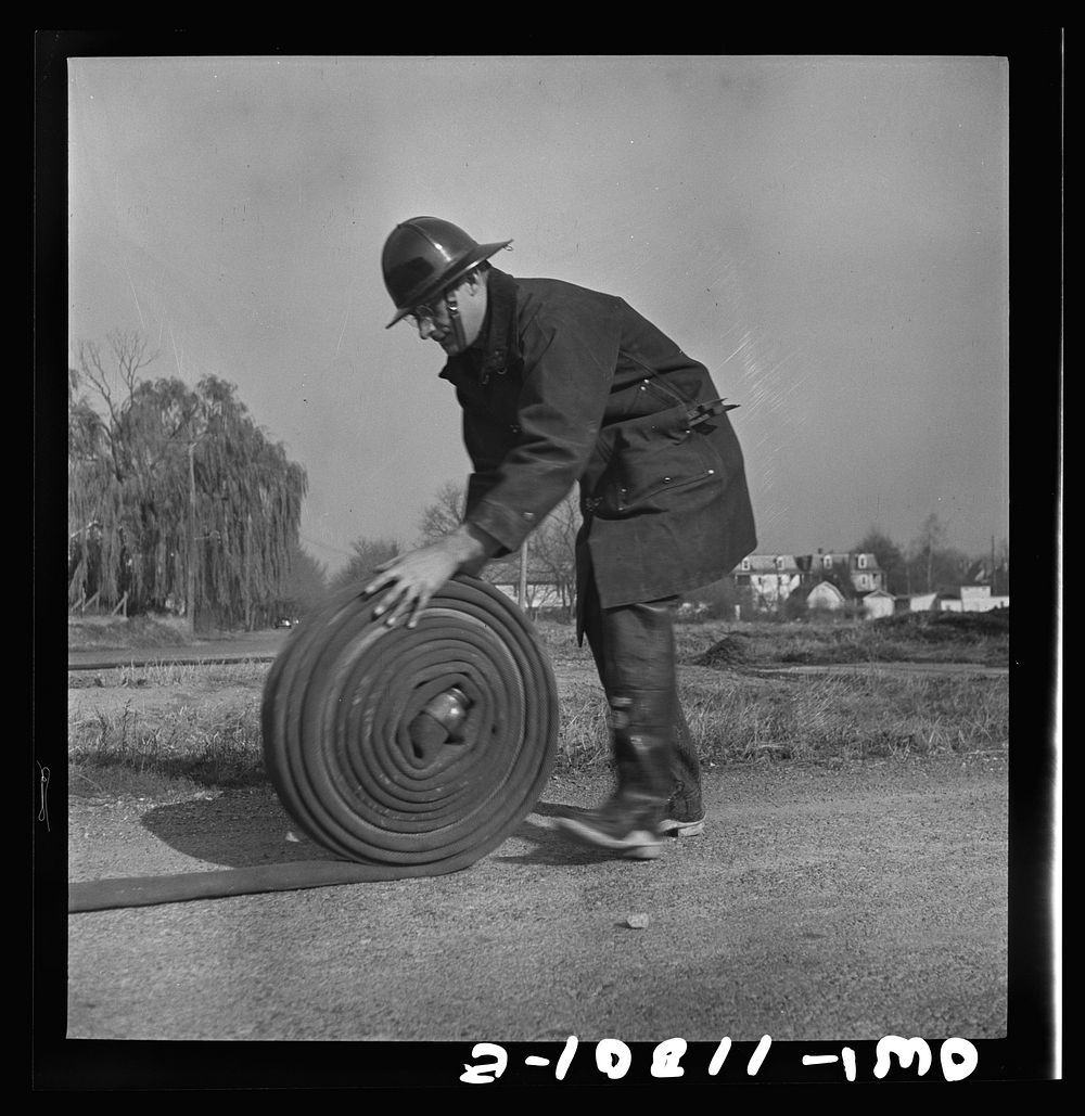 Lititz, Pennsylvania. Volunteer fireman rolling up hose during a practice air raid drill. Sourced from the Library of…