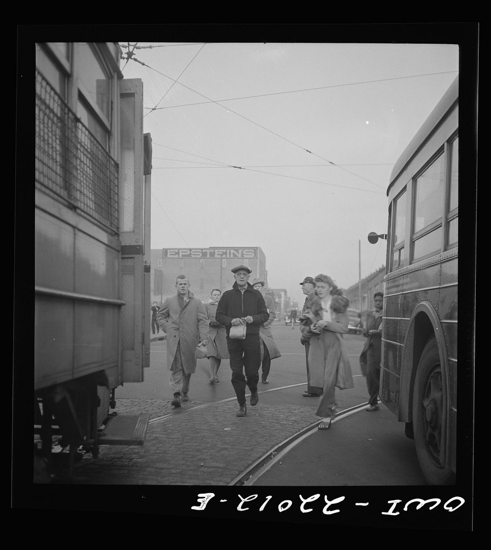 Baltimore, Maryland. Workers hurrying to catch a trolley and a trackless trolley at seven a.m.. Sourced from the Library of…