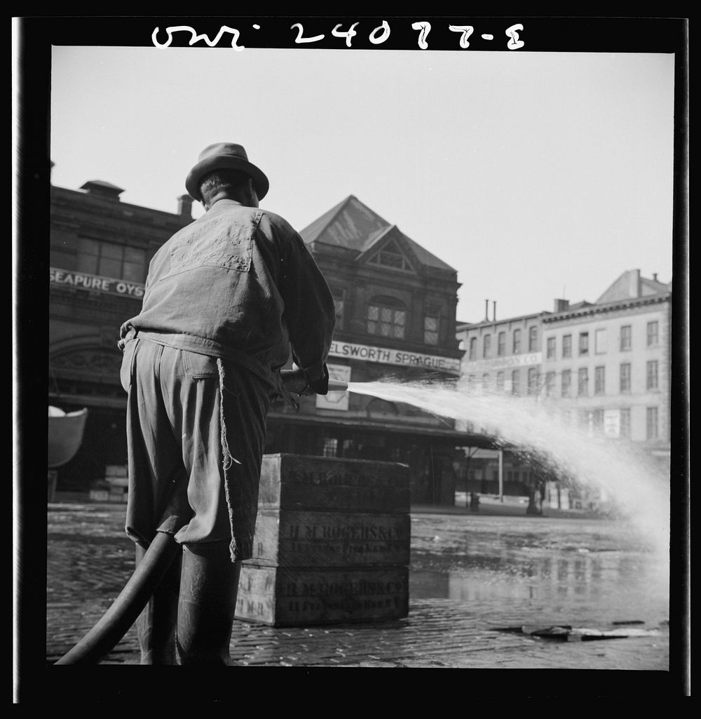 New York, New York. Workmen from the sanitary department flushing the street in front of the Fulton fish market late in the…