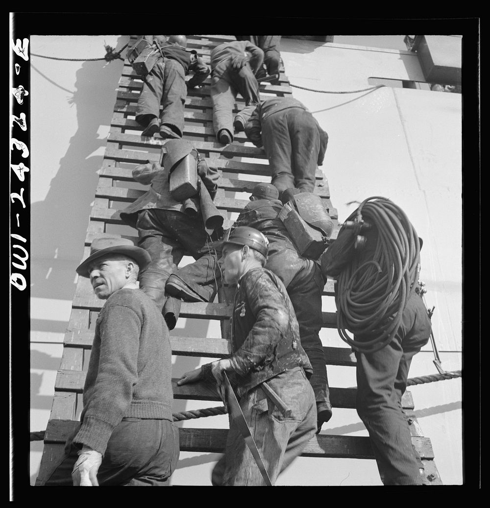 Bethlehem-Fairfield shipyards, Baltimore, Maryland. Workers on a ladder at the outfitting pier. Sourced from the Library of…