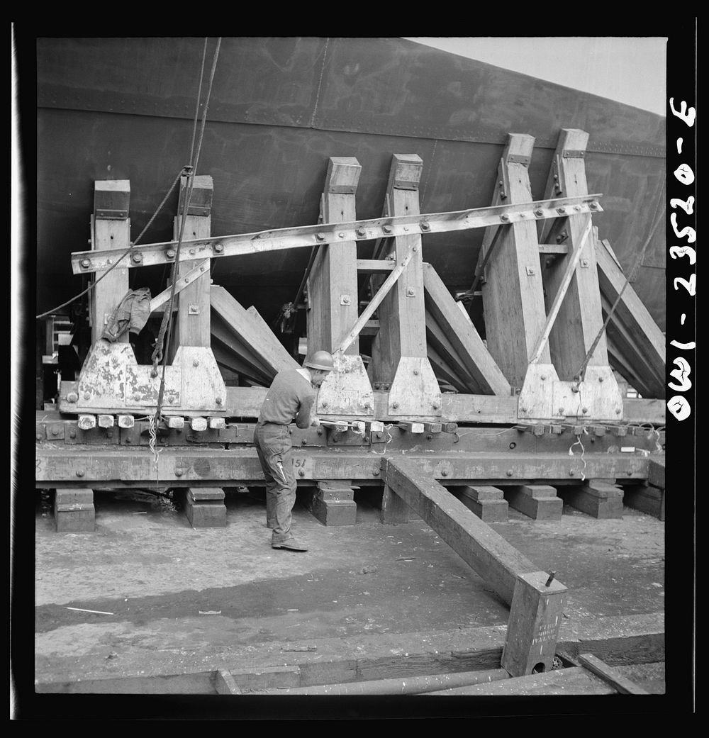 Bethlehem-Fairfield shipyards, Baltimore, Maryland. Driving wedges under a poppet before a launching. Sourced from the…