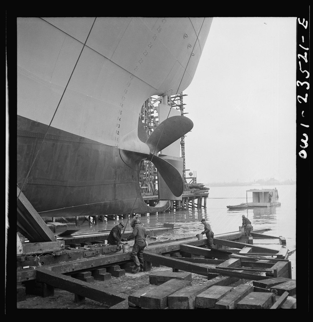 Bethlehem-Fairfield shipyards, Baltimore, Maryland. Greasing outboard end of the ways just before a launching. Sourced from…