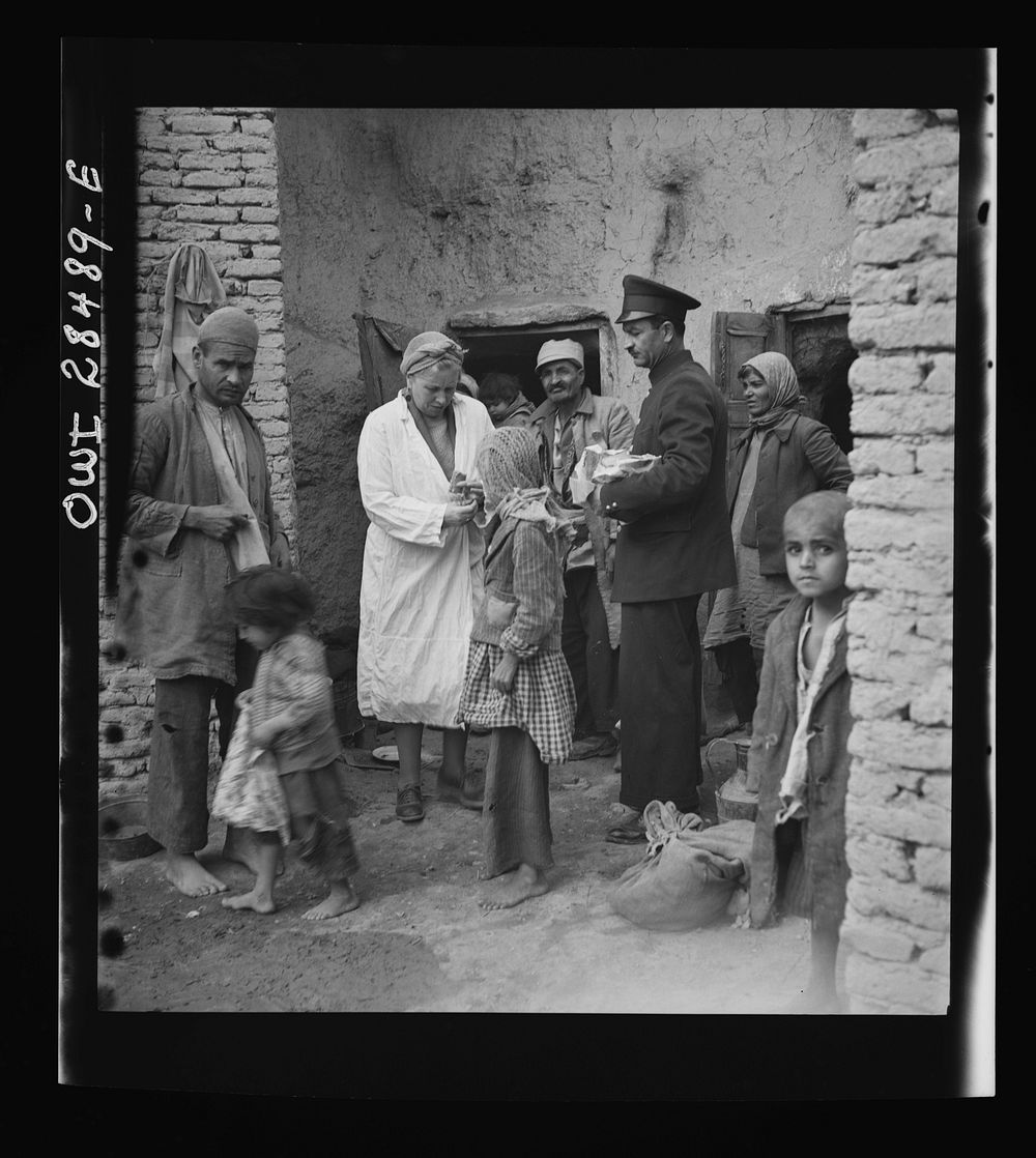 Teheran, Iran. Mrs. Louis Dreyfus, wife of the United States Minister to Iran, giving food to native children. Sourced from…