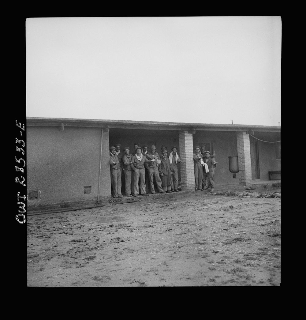American troops waiting for the rain to stop so that they can get washed at chow time. These boys work at an assembly plant…
