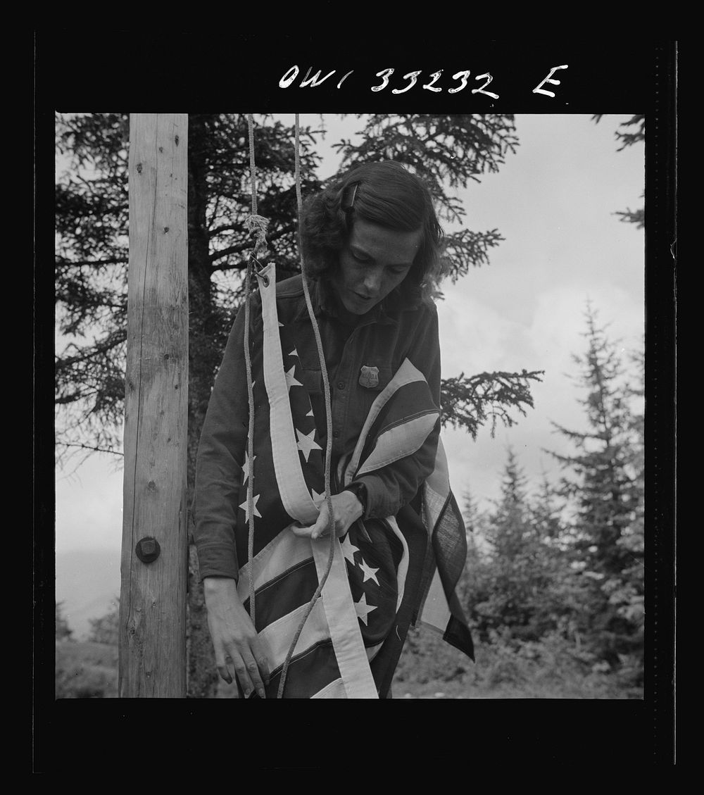 Gorham (vicinity), New Hampshire. Barbara Mortensen, a fire and airplane lookout on Pine Mountain, running up the colors.…