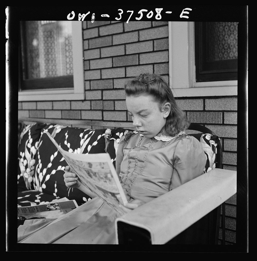 Cincinnati, Ohio. The eldest daughter of Bernard Cochran, a Greyhound bus driver, reading the Sunday funnies on the porch.…