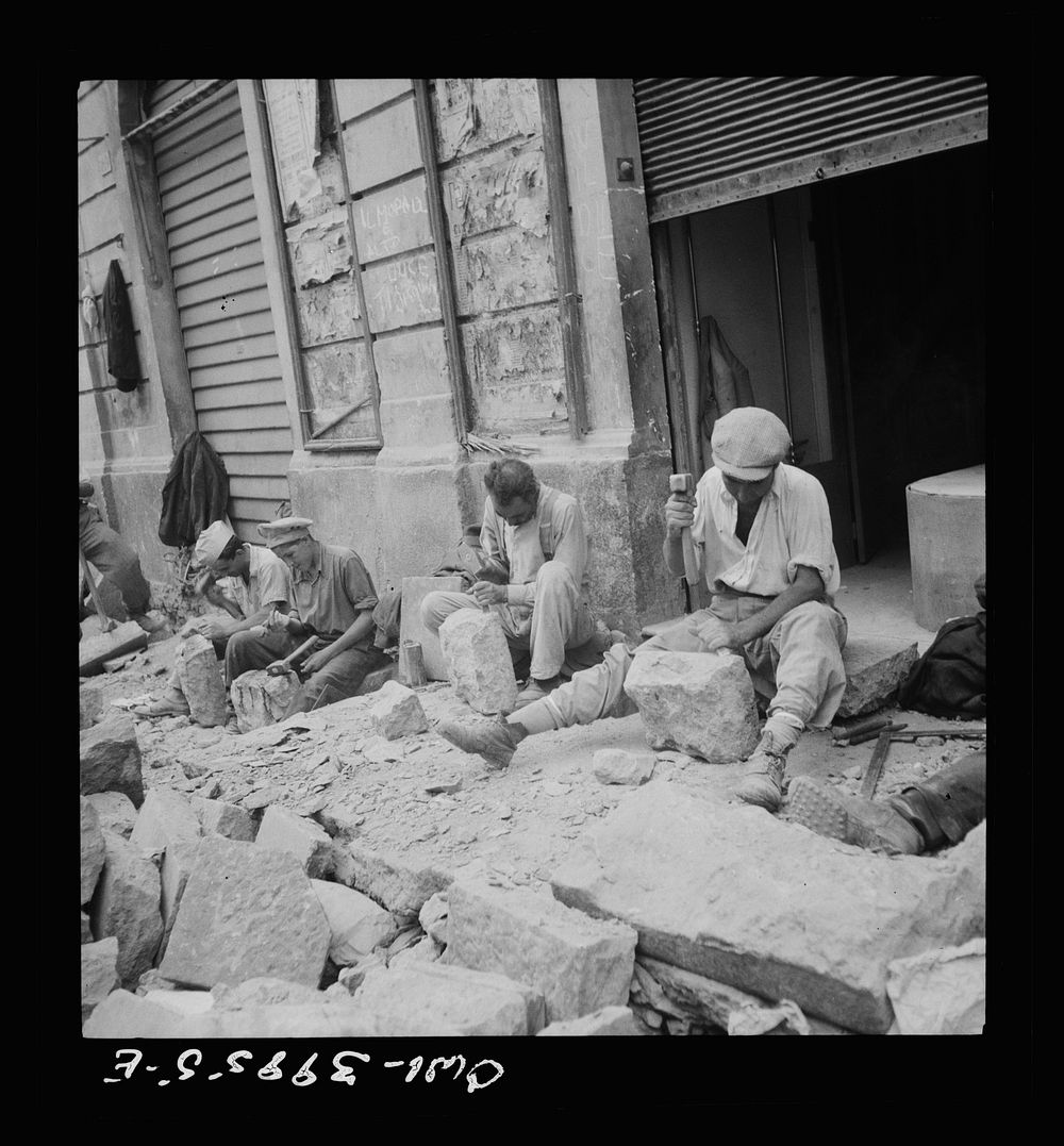 Sicilian workmen breaking stone to be used in repairing the roads demolished by the Germans in retreat. Sourced from the…