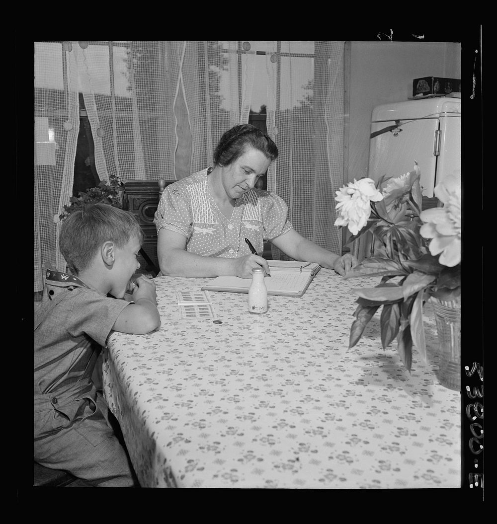 East Montpelier, Vermont. Richard, age five, son of Charles Ormsbee, shown with his mother, is licking savings stamps, a…