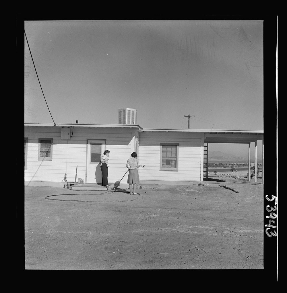 [Untitled photo, possibly related to: Las Vegas, Nevada. A worker's wife watering a newly planted lawn around one of the…
