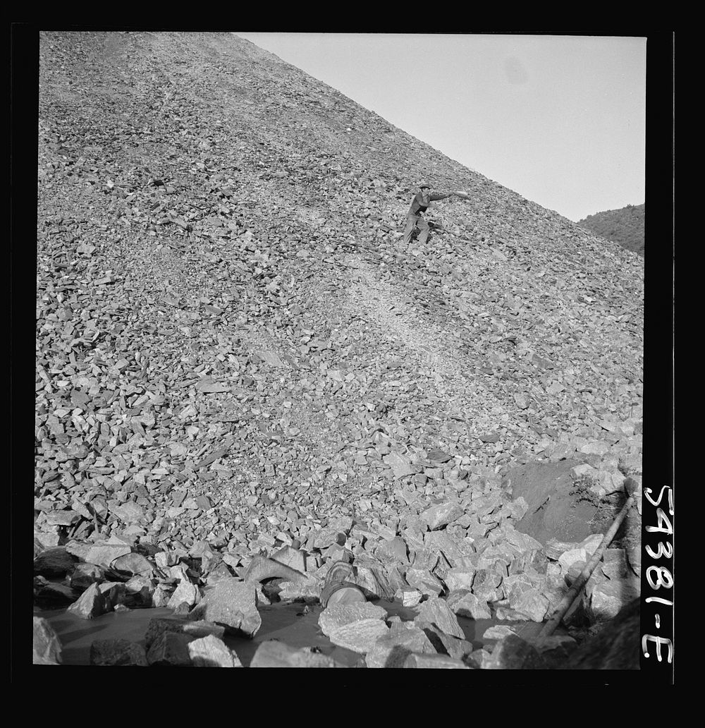 Kingman (vicinity), Arizona. A huge waste pile, showing a workman near the center picking up still valuable pieces of…
