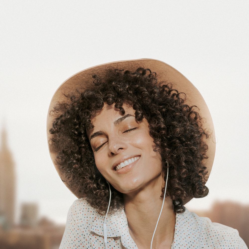 Happy woman with curly hair wearing earphones and listening to music remixed media