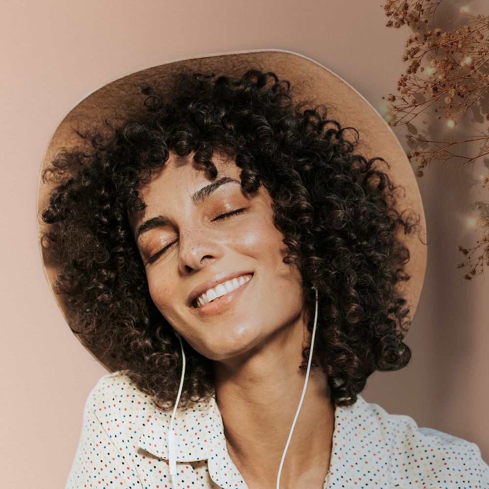 Happy woman with curly hair wearing earphones and listening to music remixed media