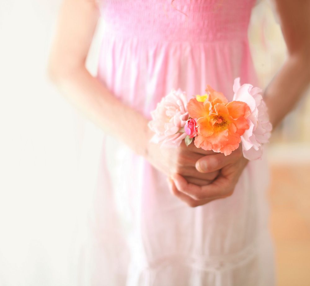 A girl holding a bouquet of white, pink and orange flowers in front of her dress. Original public domain image from…