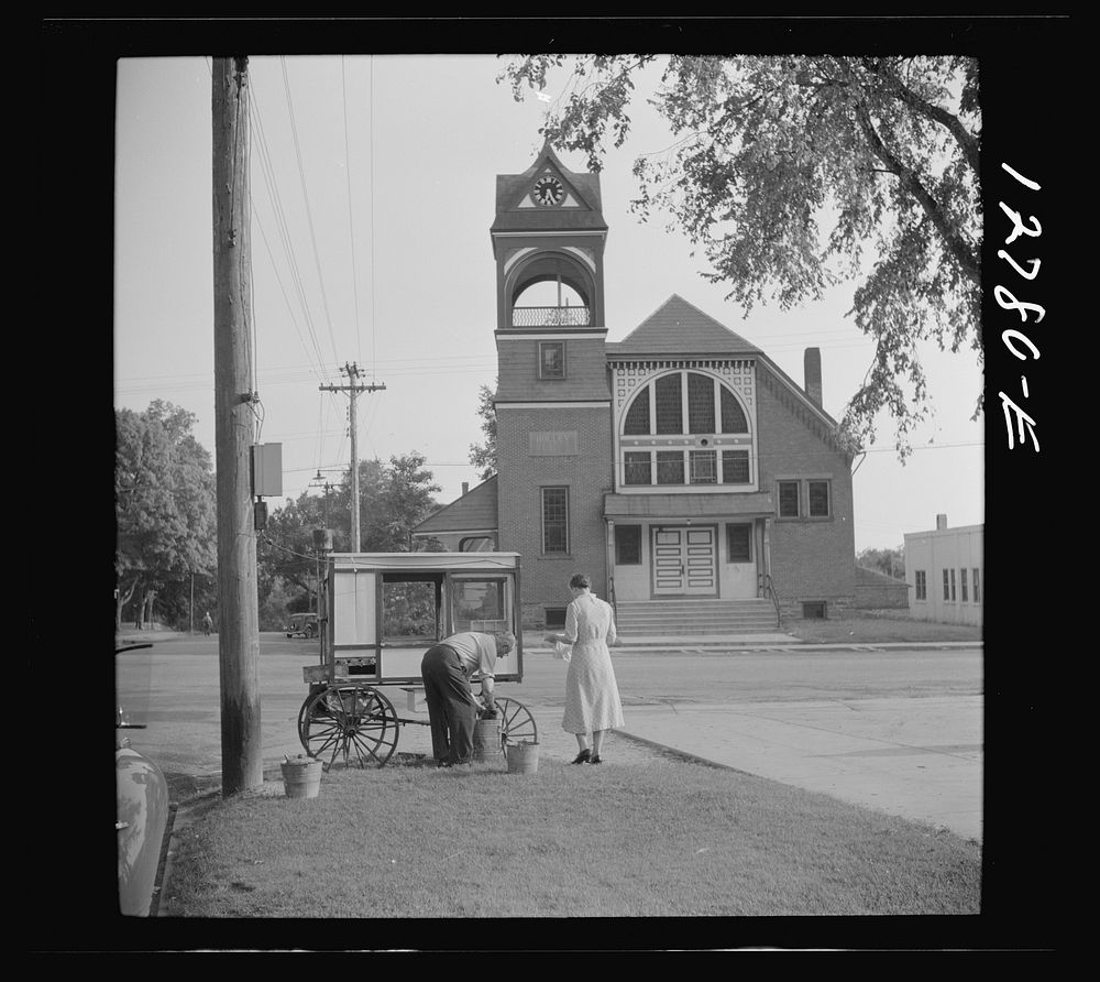 Old man and his wife preparing their popcorn roaster in front of the town hall. Bristol, Vermont. Sourced from the Library…