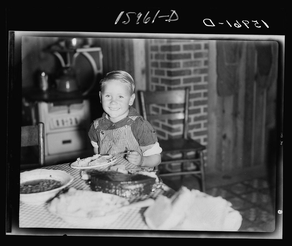 Child of former sharecropper eating at table. Southeast Missouri Farms. This is the same boy shown in negative 31215-D, two…