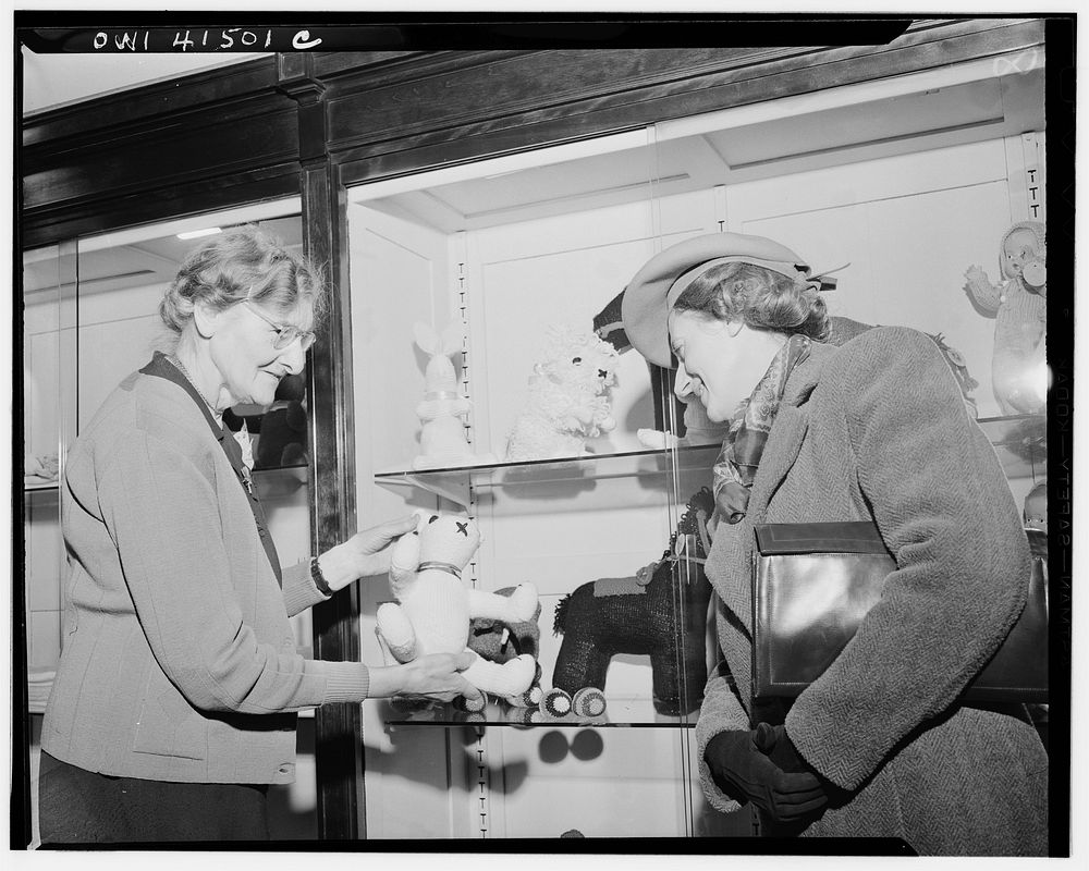 New York, New York. Miss Bloomfield, a saleslady in the Lighthouse store showing a customer knitted items for children made…