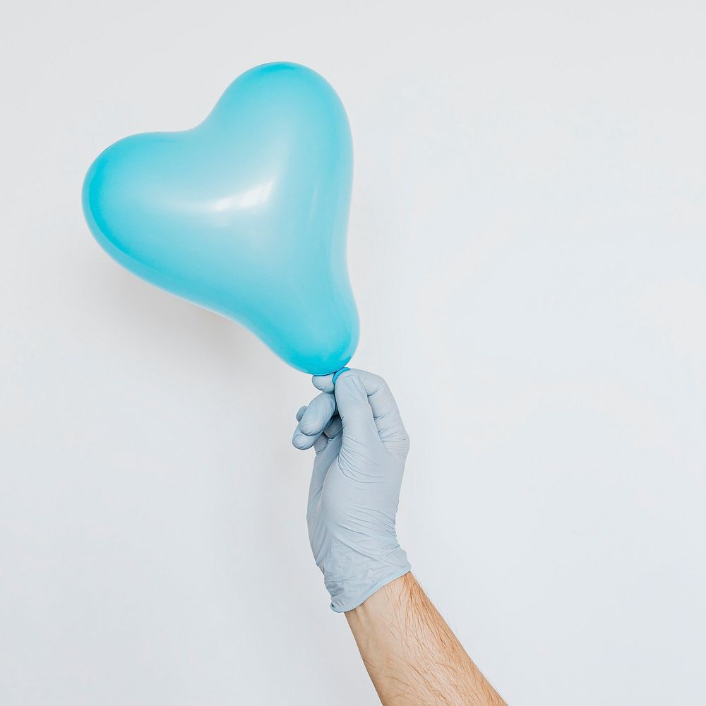 Gloved hand holding a blue heart shaped balloon on a gray background