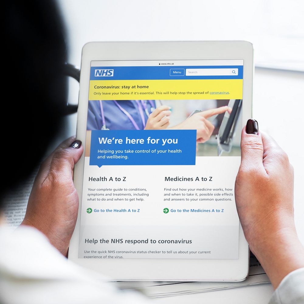 Woman reading coronavirus updates from a tablet mockup with editorial graphic from https://www.nhs.uk accessed on April 8th…
