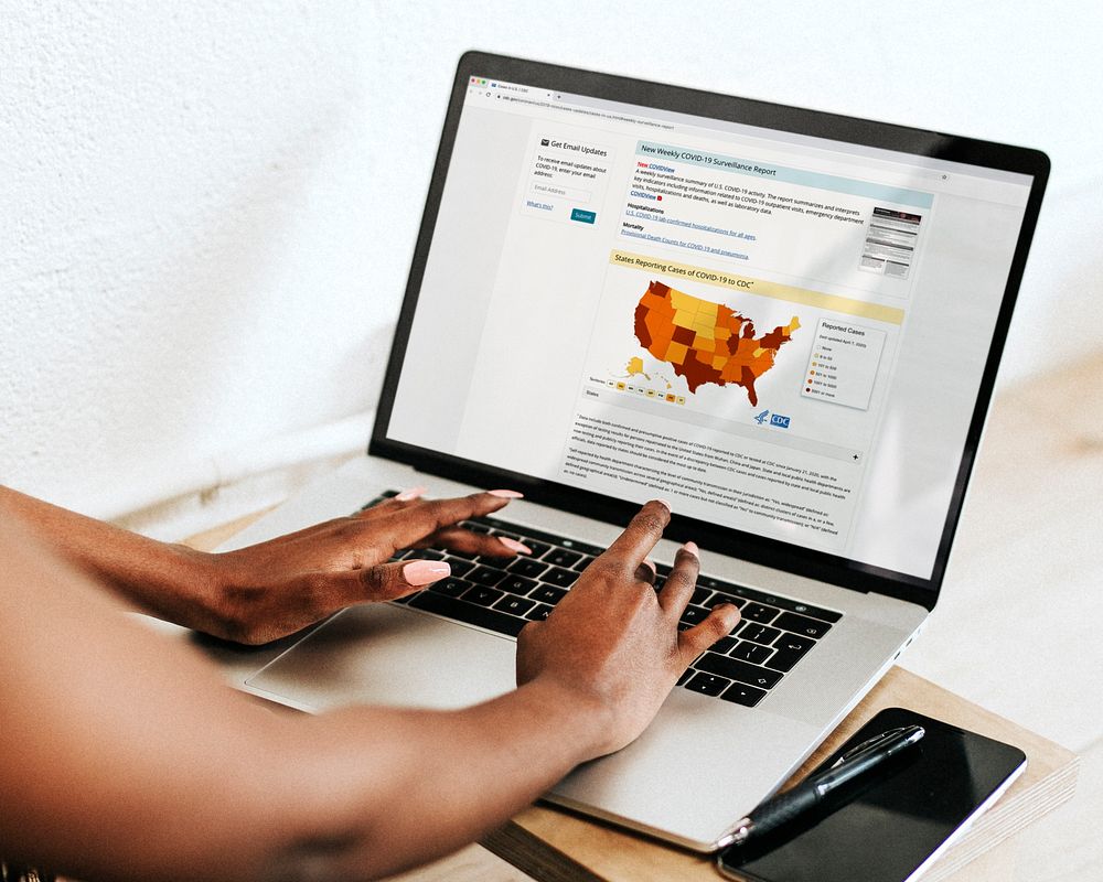 Woman reading coronavirus updates from a laptop mockup with editorial graphic from https://www.cdc.gov/coronavirus/2019…