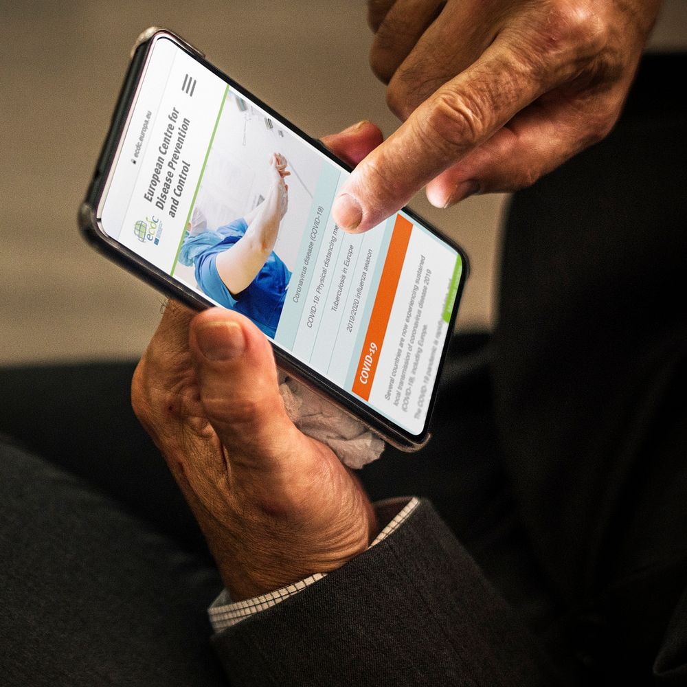 Businessman reading coronavirus information from a phone mockup with editorial graphic from https://www.ecdc.europa.eu/en…