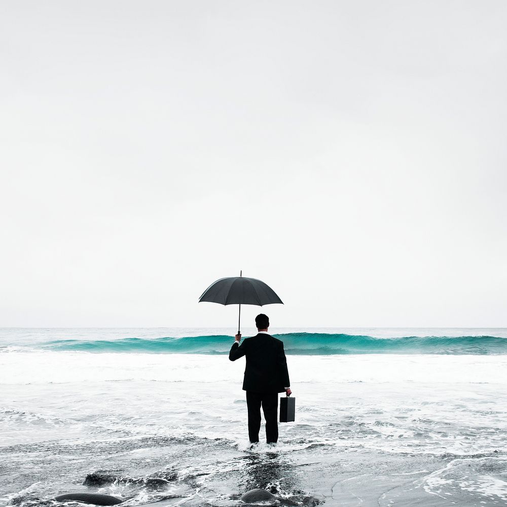 Businessman in suit with umbrella standing in sea