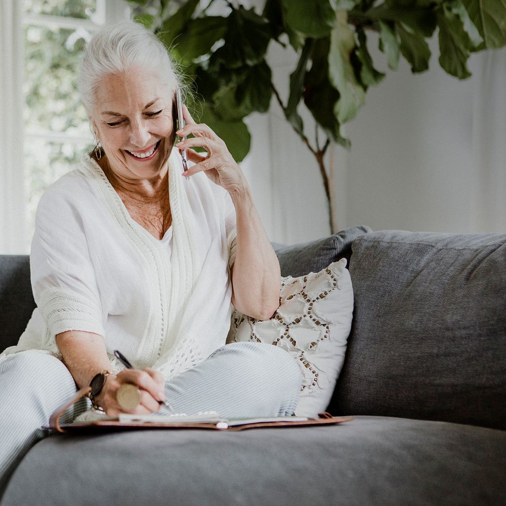 Senior businesswoman on a phone call writing on her planner at home