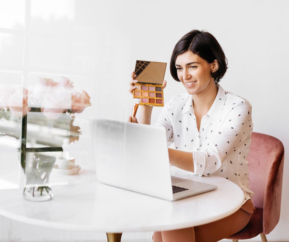 Happy women displaying an eye shadow palette with a laptop