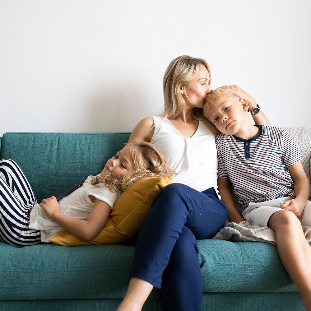 Blonde mom kissing her son&rsquo;s head and relaxing with daughter on the couch 
