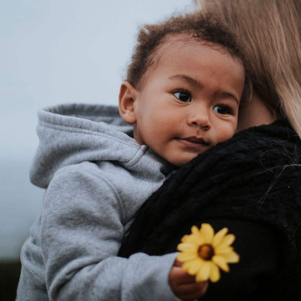Young boy holding a flower while being carried by his mom
